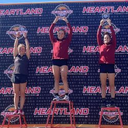 Three women stand on the podium with arms raised